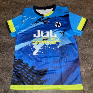 Blå fotbollströja Jul Décennie - Snygg blå fotbollströja med grafiskt mönster och tryck från Jul Décennie. Kortärmad med svarta och neongula detaljer på ärmar och nederkant. Materialet är lätt och andas, perfekt för träning eller match. Tryck på både fram- och baksida med loggor och text.