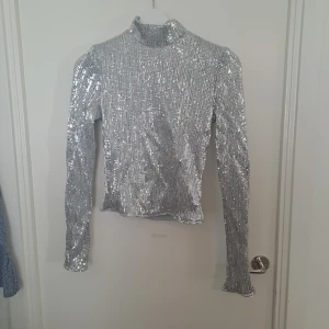 Glittrig silver polotopp  - Glittrig silverfärgad polotopp från NLY Trend i storlek 36. Dragkedja back med spänne. 🩷 finns någon lös tråd på. 