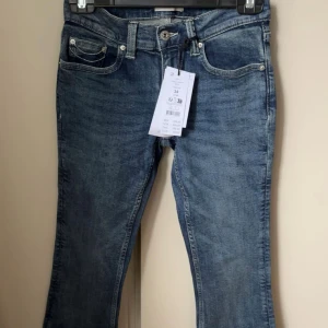 Ultra low bootcut jeans blå, stl 34 - Snygga ultra low bootcut jeans i djupblå tvätt med vita kontrastsömmar på bakfickorna. Klassisk femficksmodell med låg midja och bootcut-ben. Aldrig använda med prislapp kvar, köpta för 499 men säljer för 399✨ 