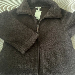 Brun teddyjacka med dragkedja - Mysig brun teddyjacka från H&M i storlek S. Jackan har hög krage, hel dragkedja framtill och två stora fickor. Perfekt för kyliga dagar och har en riktigt skön, fluffig känsla tack vare teddy-materialet.
