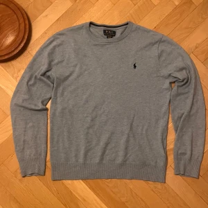 Ralph lauren tröja - Snygg grå tröja från Polo Ralph Lauren i 100% bomull. Klassisk rund halsringning, ribbade muddar och diskret broderad logga på bröstet. Perfekt för dig som gillar stilrena och tidlösa plagg. Tröjan sitter som S. Och är mer ljusblå i verkligheten än på bilderna