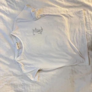 Vit Juicy Couture t-shirt med strass - Vit t-shirt från Juicy Couture i mjuk bomull. Klassisk rund hals och korta ärmar. På bröstet finns ett snyggt Juicy Couture-logo i silverfärgade strass-stenar som ger extra bling.  Aldrig använd, skickas samma dag och mer bilder kan ordnas Mvh!