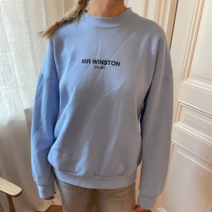 Ljusblå sweatshirt från Mr Winston - Säljer en ljusblå sweatshirt från Mr Winston med svart text. Tröjan har en relaxed passform, rund halsringning och är tillverkad i mjuk bomullsmix. Perfekt för chill dagar och enkel att styla med jeans eller mjukisbyxor.
