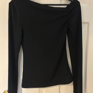 Svart tröja från Bik Bok i storlek S - Säljer en svart långärmad polotopp från Bik Bok i storlek S. Toppen har en snygg omlott-detalj vid axeln som ger en cool asymmetrisk look. Materialet är mjukt och stretchigt, perfekt för att skapa en stilren outfit. Passformen är normal och toppen är enfärgad. Super snygg. Ej andvänd!