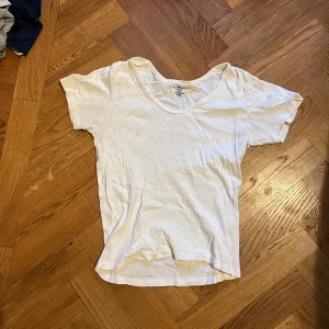 Vit ribbad t-shirt med v-ringning - Vit t-shirt från brandy melville med ribbad struktur och v-ringad hals. Modellen är kortärmad och har en klassisk, enkel passform som funkar till allt. Tillverkad i mjuk bomull för en skön känsla hela dagen.