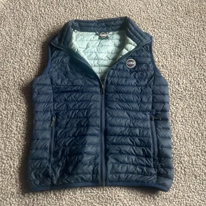 Mörkblå dunväst från Colmar - Snygg mörkblå dunväst från Colmar med quiltad design och dragkedja framtill. Västen har två praktiska sidofickor med dragkedja och ett rundat Colmar-märke på bröstet. Insidan är ljusblå och materialet är lätt och smidigt, perfekt för lager-på-lager. Passar dig mellan 160~175. Inga defekter ✅Nypris: 1250kr. 😳MITT PRIS: 500kr😍Har DU frågor kring västen är det bara att hojta till!😇MVH SWISSWEAR 🇨🇭🍾🏔️