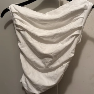 Vit oneshoulder topp med drapering - Snygg vit oneshoulder topp med cool draperad effekt framtill. Toppens tyg faller i mjuka veck och ger en trendig look. Aldrig använt men köpt förra året 