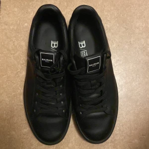 Balmain skor - Stilrena svarta sneakers från Balmain Paris med klassisk rund tå och platt sula. Skorna är i skinn och har snörning framtill samt diskret Balmain-logga på plösen. Kommer med originalkartong och dustbag. Perfekta för dig som gillar exklusiva och minimalistiska sneakers. Vet inte varför det står H&M men det ska stå balmain!