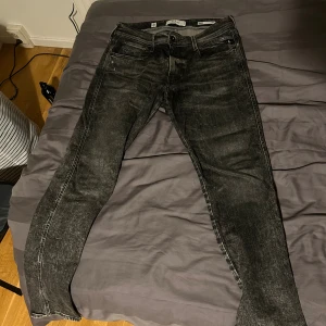 Replay Anbass svarta slim jeans - Säljer ett par Replay Anbass slim fit jeans i svart tvättad denim. Jeansen har klassisk femficksdesign, smal passform och snygga slitningar för en cool look. Perfekta för dig som gillar stilrena och moderna jeans med lite edge. Slitning finns i skrevet men inte så farligt