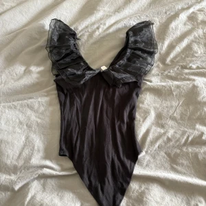 Svart volangbikini från Musica - Supersnygg svart bikini från Musica med djup v-ringning och stora volangärmar i transparent tyg. Bikinin har en tight passform och är perfekt för dig som vill sticka ut på stranden. Materialet känns mjukt och följsamt mot kroppen.