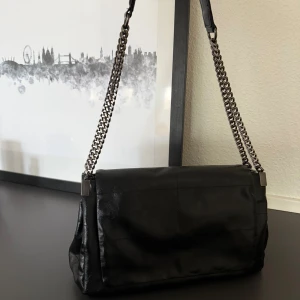 Svart axelväska i skinn med kedjerem från Zara  - Stilren svart axelväska i mjukt skinn med silverfärgad kedjerem. Väskan har flera fack inuti, inklusive ett med dragkedja, och stängs med magnetlås