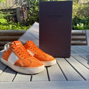 Valentino Garavani orange sneakers mocka - Snygga sneakers från Valentino Garavani i orange mocka med vita skinnpaneler och vita detaljer på häl och sula. Klassisk låg modell med snörning och rund tå. Kommer med originalkartong och dustbag. Perfekta för dig som vill sticka ut med exklusiva skor. OBS EXTRA NITAR TILLKOMMER!