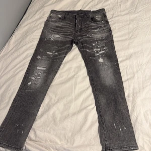 Grå slitna jeans från Dsquared2 - Snygga grå jeans från Dsquared2 med slitna detaljer och distressed look. Jeansen har raka ben, klassisk femficksdesign och coola slitningar framtill och baktill. Tillverkade i bomull med en trendig, mörkgrå tvätt och patch med '1964' på linningen.