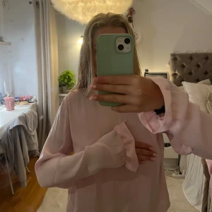 Ljusrosa blus med volang från NA-KD - Supersöt ljusrosa blus från NA-KD i storlek 36. Blusen har långa ärmar, volangdetaljer vid halsringningen