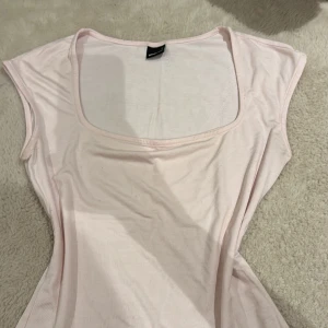 Ljusrosa topp med fyrkantig ringning - Supersöt ljusrosa topp från Gina Tricot i mjuk bomull. Toppen har en fyrkantig ringning och är ärmlös med en figurnära passform. Perfekt att styla med jeans eller kjol för en fräsch look.