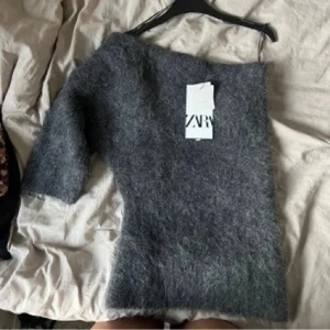 Grå stickad oneshoulder tröja - Säljer denna super populära, fluffiga grå:a stickade tröjan med oneshoulder-design och trekvartsärm. Perfekt för dig som gillar att sticka ut med en cool och annorlunda look. Mjuk och skön, passar till jeans eller kjol. OBS sitter som en S!