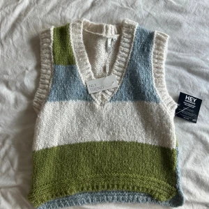 Randig stickad väst från NLY Trend - Supermysig stickad väst från NLY Trend i storlek XS. Västen har breda ränder i vitt, ljusblått och olivgrönt, samt en djup v-ringning och ribbade kanter. Perfekt att slänga över en skjorta eller t-shirt för en trendig lager-på-lager-look.