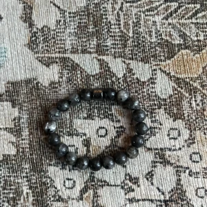 Gråsvart pärlarmband med metallpärla från sayless  - Stilrent armband med runda pärlor i gråsvart stenlook och en metallisk detaljpärla. Elastisk tråd gör det enkelt att ta på och av. Perfekt accessoar för dig som gillar en cool och minimalistisk stil.