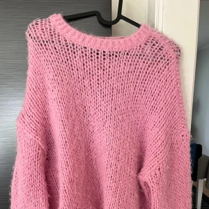 Ljusrosa stickad tröja med oversized passform - Supermysig ljusrosa stickad tröja med grovstickat mönster och oversized passform. Tröjan har långa ärmar och bred halsringning, perfekt för lager på lager. Den fluffiga känslan gör den extra cozy under kyliga dagar. Den är ljusare rosa i verkligheten 