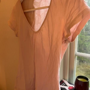 Ljusrosa t-shirt med v-ringning Esprit - Supersöt ljusrosa t-shirt från Esprit med djup v-ringning och lätt rynkdetalj framtill. Modellen är kortärmad och i mjuk bomull, perfekt för en chill och enkel look. Passar dig som gillar basic men ändå vill ha en liten twist på toppen.