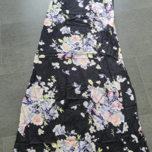 Blommig långklänning från Gina Tricot - Supersnygg långklänning från Gina Tricot i svart med blommigt mönster i pastelliga färger som lila, rosa och ljusgrön. Klänningen har smala axelband och är tillverkad i mjuk viskos som känns lätt och luftig. Perfekt för dig som vill sticka ut med en romantisk vibe.