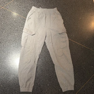 Grå cargopants från A Bathing Ape - Snygga grå cargopants från A Bathing Ape med broderad logga på benfickan. Byxorna har elastisk midja med snörning, flera fickor inklusive stora cargofickor på sidorna och muddar vid bensluten. Tillverkade i mjuk bomull för maximal komfort.