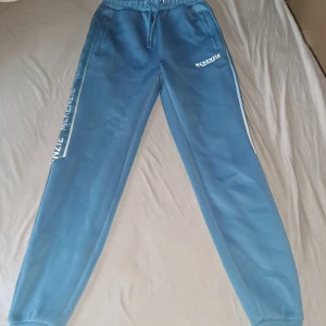 Blå mjukisbyxor från McKenzie XS - Snygga blå mjukisbyxor från McKenzie i storlek XS. Byxorna har resår och snörning i midjan, dragkedjefickor och tryckt logga längs benet. Perfekta för chill eller träning, med skön passform och sportig look.