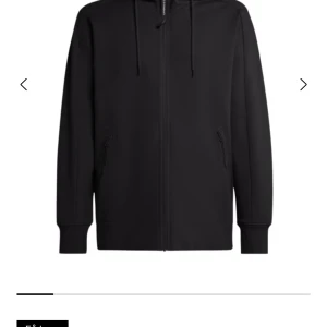 Svart hoodie med dragkedja, storlek L C.P company  - Svart hoodie i storlek L med hel dragkedja framtill och två fickor med dragkedja. Tröjan har huva med snörning och är tillverkad i mjuk bomull. Perfekt för en chill och stilren look.