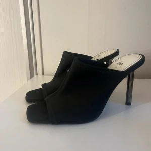 Svarta klackar med öppen tå från Zara - Snygga svarta klackar från Zara med öppen tå och fyrkantig front. Skorna har hög klack i metall och en stilren, minimalistisk design. Perfekta för dig som vill sticka ut med en modern och trendig look.