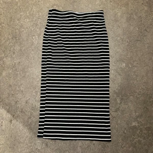 Svartvit randig kjol - Säljer en svartvit randig kjol i midilängd med raka linjer och stretchigt material. Kjolen har en klassisk look med horisontella ränder och passar perfekt till en enkel topp eller hoodie. Superskön och lätt att styla för en cool vardagsstil.