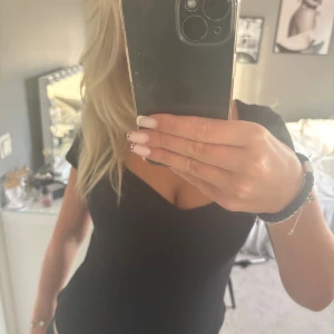 Svart v-ringad topp med kort ärm - Säljer en svart body med v-ringning och korta ärmar. Toppen har en tight passform och är enkel men snygg, perfekt att matcha med jeans eller kjol. Materialet känns mjukt och stretchigt, vilket gör den bekväm att bära hela dagen.