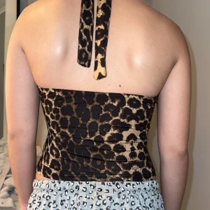 Leopardmönstrad halterneck topp - Säljer en snygg leopardmönstrad halterneck topp med omlott framtill och djup v-ringning. Toppen har knyt runt nacken och är figurnära med croppad passform. Perfekt för dig som vill sticka ut med ett djuriskt mönster!