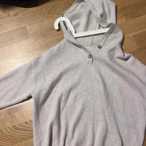 Beige hoodie från Oysho XS - Mysig beige hoodie från Oysho i storlek XS. Tröjan har huva, långa ärmar och två snygga knappar vid halsen. Tillverkad i mjuk bomullsmix som känns skön mot huden. Perfekt för chill dagar eller när du vill ha något bekvämt på dig.