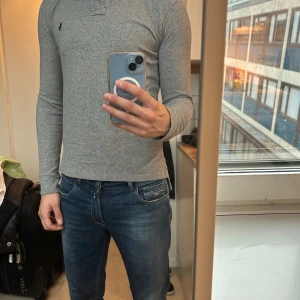 Ralph Lauren Grå långärmad pikétröja  - Grå långärmad pikétröja från Polo Ralph Lauren i custom fit. Klassisk krage, knäppning med två knappar och broderad logga på bröstet. Mjuk och skön bomullskvalitet, perfekt till jeans eller chinos.