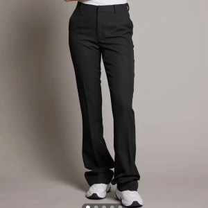 Svarta kostymbyxor  - Snygga svarta kostymbyxor med klassisk passform och bootcut ben. Byxorna har pressveck, hällor för bälte och stängs med dragkedja och knapp. Perfekta för en clean och stilren look. Materialet känns mjukt och följsamt.