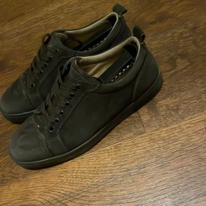 Svarta sneakers från Christian Louboutin - Säljer ett par svarta sneakers från Christian Louboutin med klassisk röd sula. Skorna har snörning, rund tå och är tillverkade i skinn. Perfekta för dig som vill ha en stilren och lyxig look med en ikonisk touch.