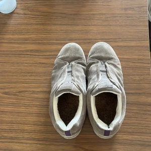 Beige mockasneakers från Eytys - Säljer ett par beige sneakers från Eytys i mjuk mocka med vit sula och elastisk detalj över vristen. Skorna har en chunky platt sula och rund tå, samt diskret logga på plösen. Perfekta för dig som gillar stilrena och bekväma sneakers med lite extra edge.