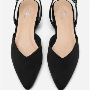 Svarta ballerinaskor från Clou - Snygga svarta ballerinaskor från Clou med spetsig tå och öppen häl. Skorna har en smal rem med spänne runt hälen och är gjorda i mockaliknande material. Perfekta för dig som gillar stilrena och eleganta skor med en modern touch. Skorna är endast använda 1 gång. 