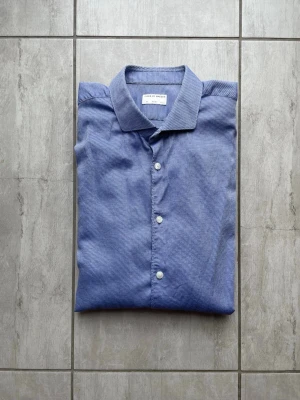 Blårandig skjorta Tiger of sweden  - Snygg blå skjorta från tiger of sweden med smala vita ränder. Klassisk krage, vita knappar framtill och långa ärmar med manschett. Tillverkad i mjuk bomull som känns skön mot huden. Perfekt för dig som gillar stilrena och tidlösa plagg. Vid frågor och funderingar skriv gärna!