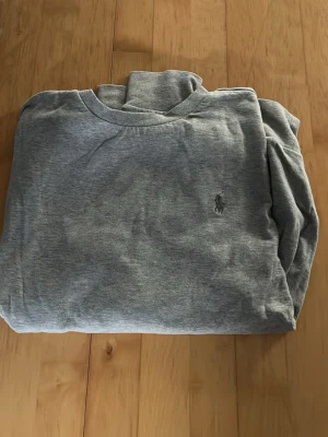 Grå sweatshirt från Ralph Lauren - Klassisk grå sweatshirt från Ralph Lauren, lite tunnare tröja med rund halsringning och den ikoniska broderade loggan på bröstet. Tillverkad i mjukt bomullsmaterial som är skönt att bära. Enkel och stilren design som passar till det mesta. Storlek S. Skriv för frågor eller fler bilder, pris kan diskuteras.