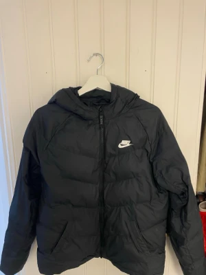 Svart pufferjacka från Nike med huva - Säljer en svart pufferjacka från Nike med huva och storleken är 158-170cm. 