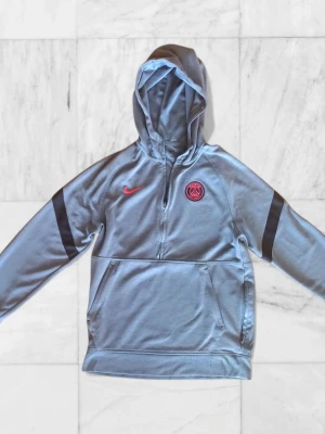 PSG Nike hoodie - Snygg PSG quarter zip-hoodie från Nike i storlek S. Har mest legat i garderoben och inte använts på ett tag. Plagget är i fint skick överlag finns en liten blå fläck och Nike broderiet på loggan är lite snett, men inget som märks när man har den på. Väldigt bekväm och lätt att styla. Är flexibel med priset