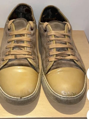 Bruna sneakers med mockadetaljer - Snygga bruna sneakers med ovandel i mocka och tåparti i beige gummi. Skorna har beige snörning och klassisk låg modell. Perfekta för dig som gillar en stilren och avslappnad look.