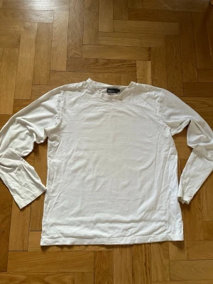Vit långärmad tröja  - En basic vit långärmad tröja. Tröjan har rund halsringning och är gjord i mjukt bomullstyg. Perfekt att styla lager på lager eller bära som den är. En fläck mitt på tröjan som går bort i tvätten. Längd: 62 Bredd: 51