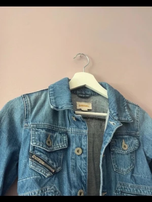 Blå jeansjacka från Diesel - Snygg blå jeansjacka från Diesel med klassisk krage, knappstängning och flera fickor framtill. Jackan har en cool detalj med dragkedja på ena bröstfickan och är figursydd för en modern look.
