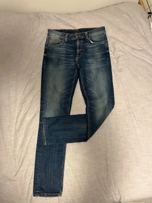 Blå jeans från Nudie Jeans - Hej! Säljer ett par blåa jeans från Nudie Jeans med snygg tvätt och snygga detaljer. De är i väldigt bra skick och har size 32W 34L.