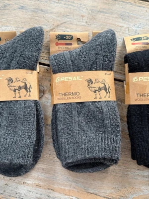 Gråa ullstrumpor från Pesail - Mysiga och varma gråa ullstrumpor från Pesail, perfekta för kalla dagar. Strumporna är ribbade och tillverkade i ullblandning med 90 procent ull för extra värme. Märkta som thermo och passar storlek 43-47. 