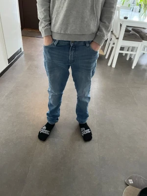 Blå raka jeans i klassisk modell - Säljer ett par blå jeans med rak passform och klassisk femficksdesign. Jeansen har en ljus tvätt och subtila slitningar framtill för en avslappnad look. Perfekta till vardags och lätta att matcha med olika stilar.