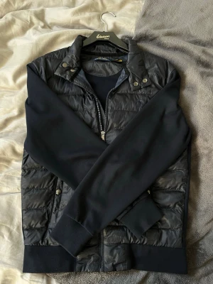 Svart cardiganjacka från Polo Ralph Lauren - Stilren marinblå cardiganjacka från Ralph Lauren med quiltad framsida och mjuka ärmar i sweatshirtmaterial. Jackan har dragkedja, tryckknappar vid kragen och ribbade muddar vid ärmslut och nederkant. Perfekt för våren! Bara att höra av sig vid intresse🌟💫