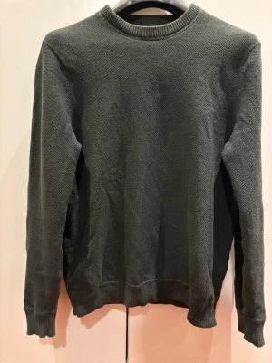 Mörkgrön stickad tröja - En enkel och stilren mörkgrön stickad tröja med rund halsringning och ribbade muddar vid ärmslut och nederkant. Perfekt för lager-på-lager och passar till det mesta. Materialet känns mjukt och bekvämt.